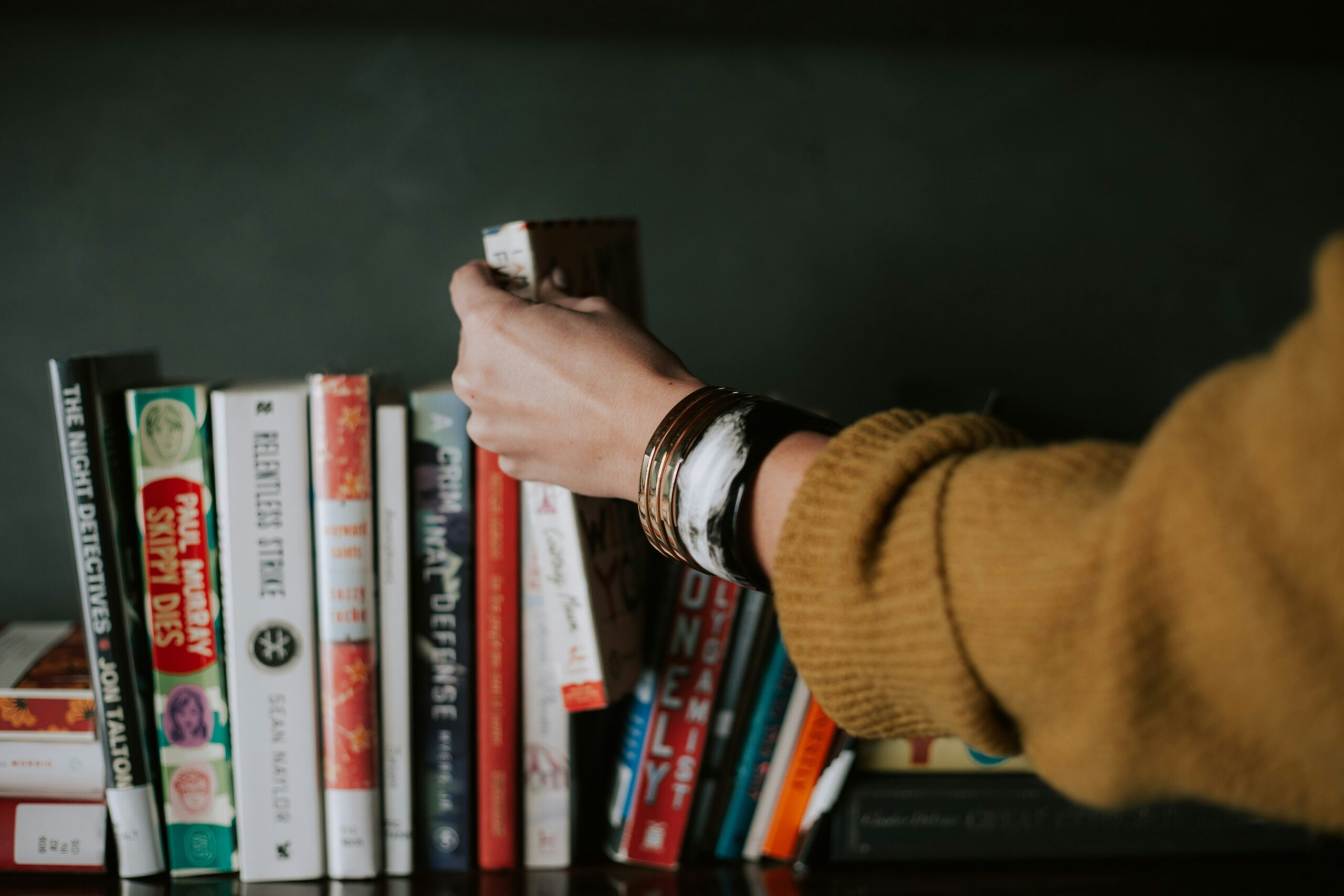 Hand grabbing a book from a shelf, symbolizing reading habit and personal growth