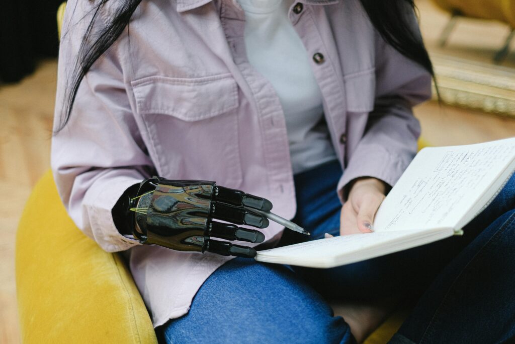 Pessoa com mão robótica segurando e escrevendo em um caderno, simbolizando a colaboração entre inteligência artificial e escrita humana