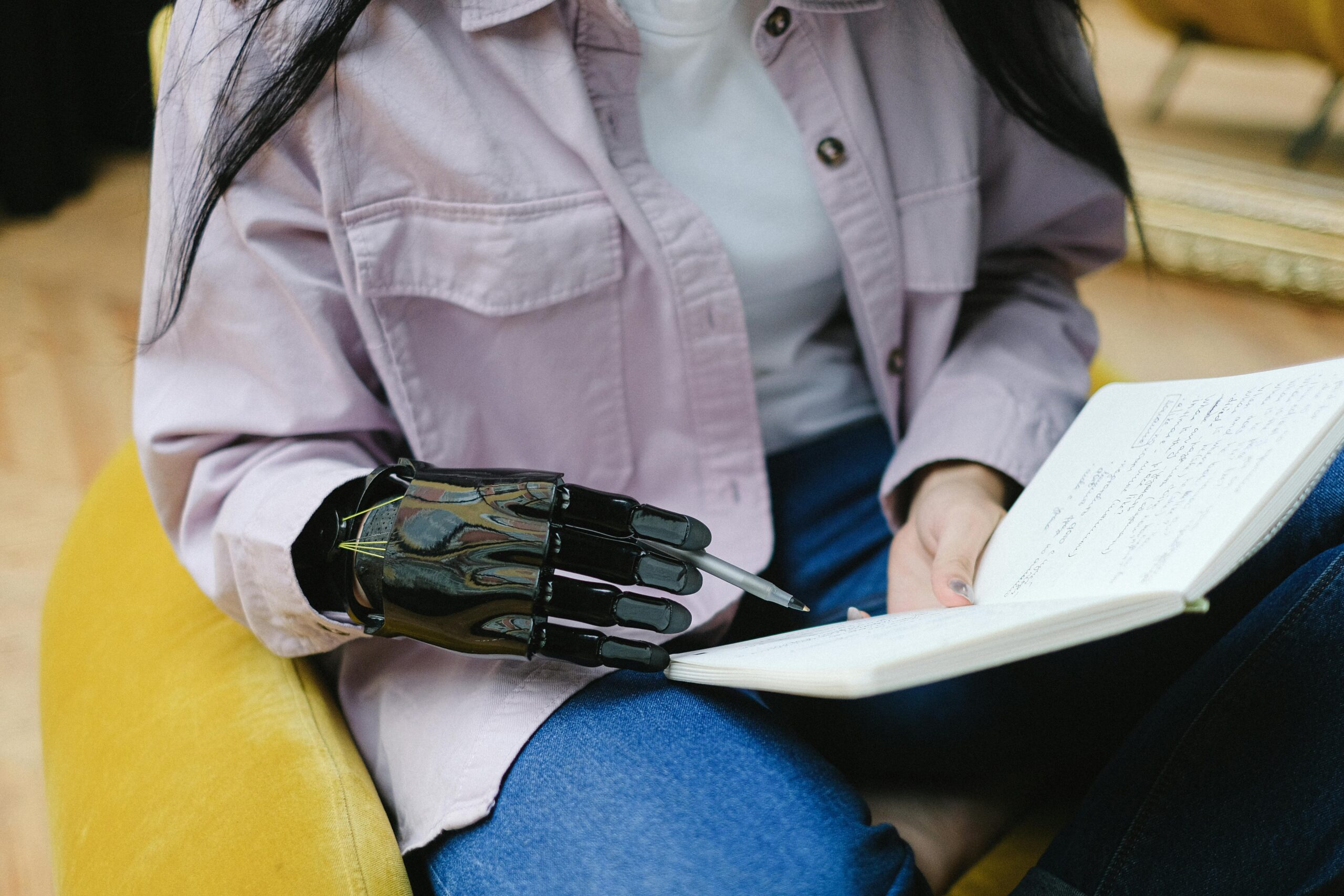 Pessoa com mão robótica segurando e escrevendo em um caderno, simbolizando a colaboração entre inteligência artificial e escrita humana